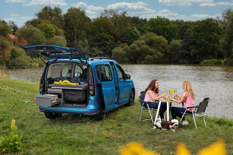 Volkswagen Caddy California na louce u řeky, s piknikovým setem židliček a stolku